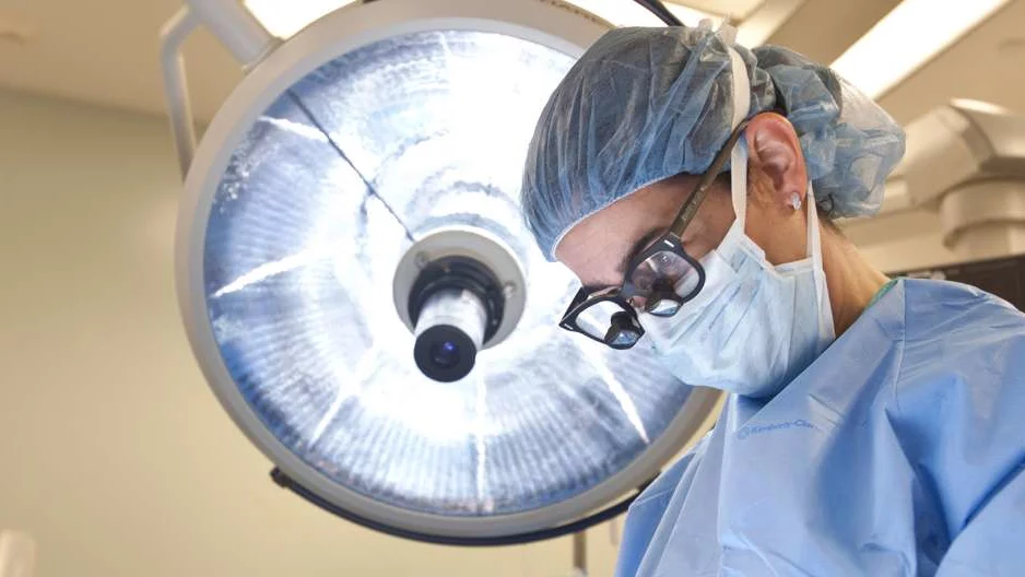 Photo of Doctor in surgery with surgical lamp behind them 